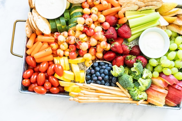 Tábua de lanches com frutas frescas, legumes, bolachas e molhos.