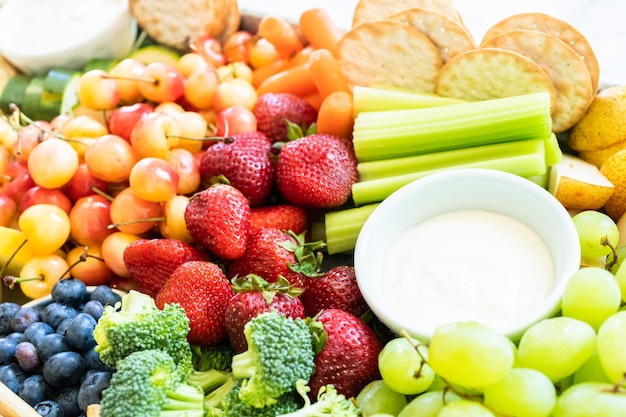 Tábua de lanches com frutas frescas, legumes, bolachas e molhos.