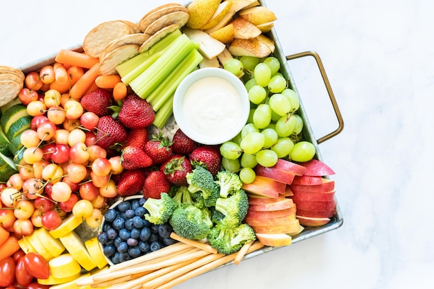 Tábua de lanches com frutas frescas, legumes, bolachas e molhos.