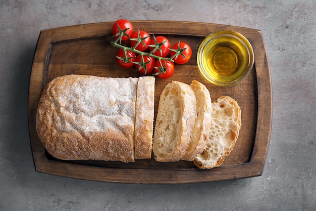 Tábua de madeira com azeite, pão fresco e tomate na mesa