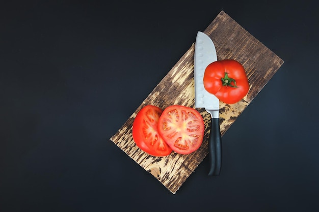 Tábua de madeira com legumes crus Tomate na tábua rústica Comida vegetariana saudável à base de plantas em fundo escuro