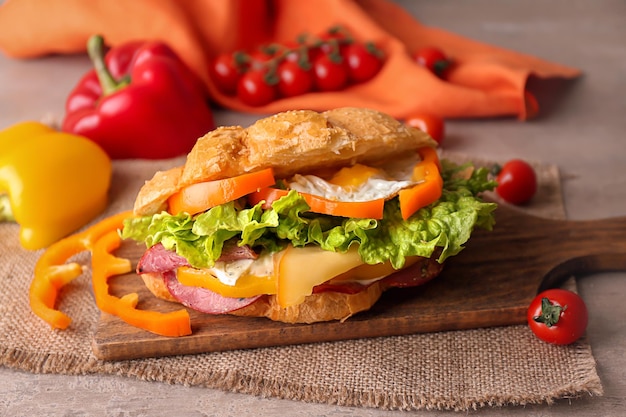 Tábua de madeira com saboroso sanduíche de croissant na mesa