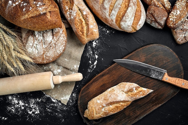 Tábua de madeira de pão fresco e faca de corte na mesa preta