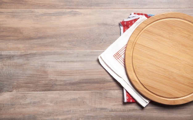 Tábua de pizza vazia e toalha de mesa de tecido no fundo de madeira.