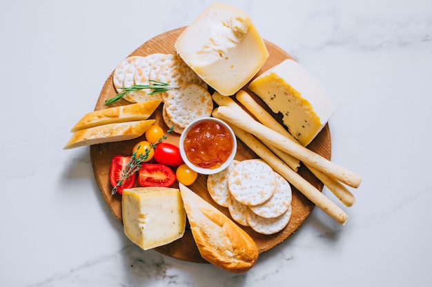 Tábua de queijos com tomate, geléia, baguete, palitos de pão e bolachas