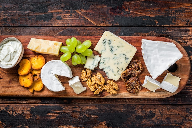 Tábua de queijos variados com Brie, Camembert, Roquefort, Parmesão, Requeijão Azul, Uva e Nozes. Fundo de madeira escuro. Vista do topo.