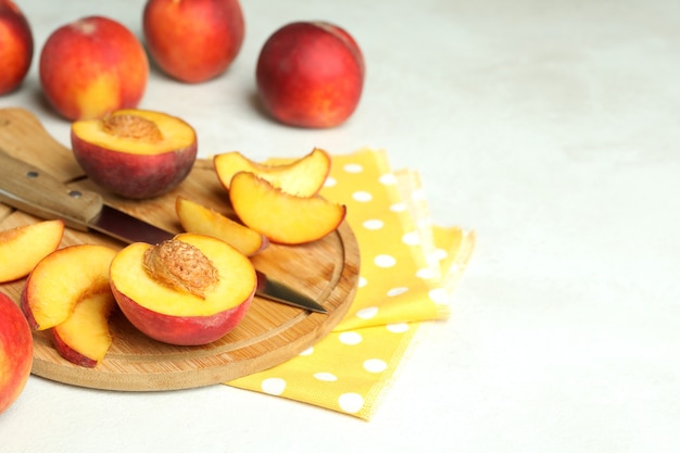 Tabuleiro com frutas pêssego, faca e pano de prato na mesa texturizada branca