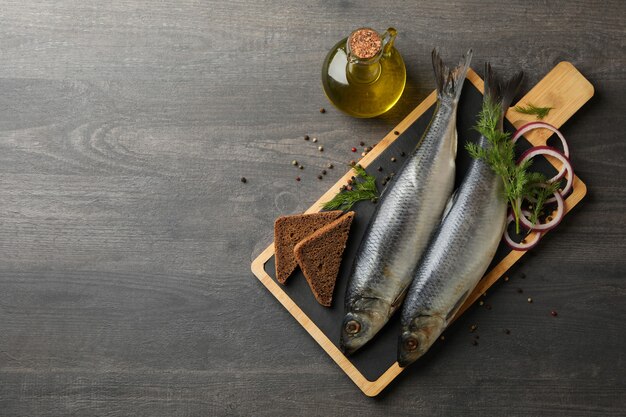 Tabuleiro com peixe arenque e especiarias e óleo no fundo escuro de madeira