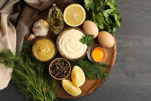 Tabuleiro com tigela de maionese e ingredientes para cozinhar em fundo escuro de madeira