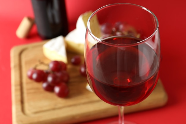 Tabuleiro com vinho, queijo e uva sobre fundo vermelho