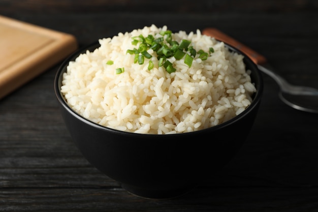 Tabuleiro, tigela de arroz delicioso e colher na superfície de madeira, close-up