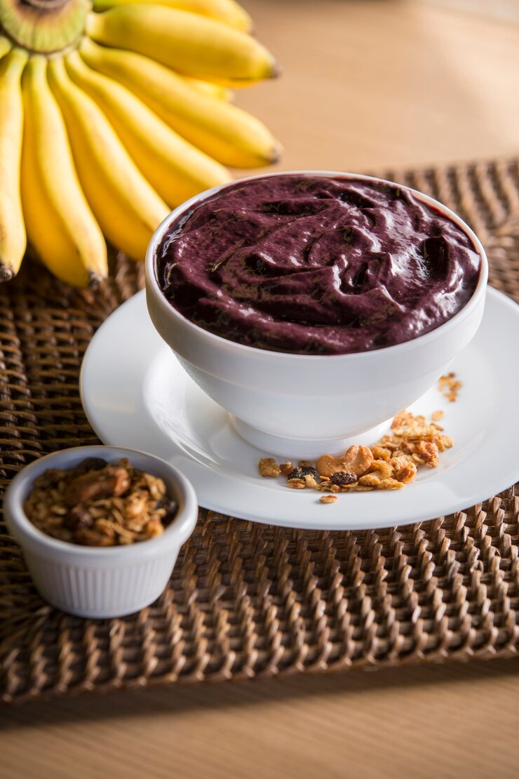 Foto taça de açaí com banana e granola em superfície rústica