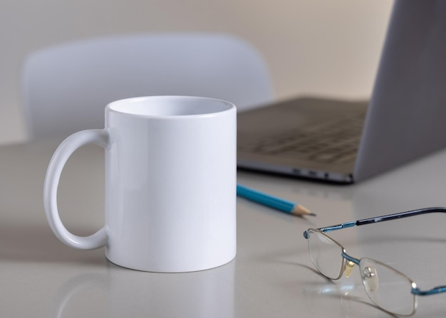 Taça de café branca em mesa de escritório cinza contra óculos de laptop e modelo de close-up de lápis