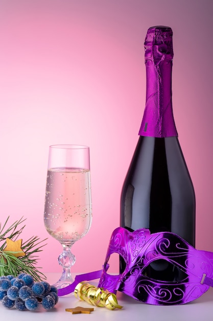 Taça de champanhe, garrafa, máscara de carnaval e ornamentos em fundo rosa