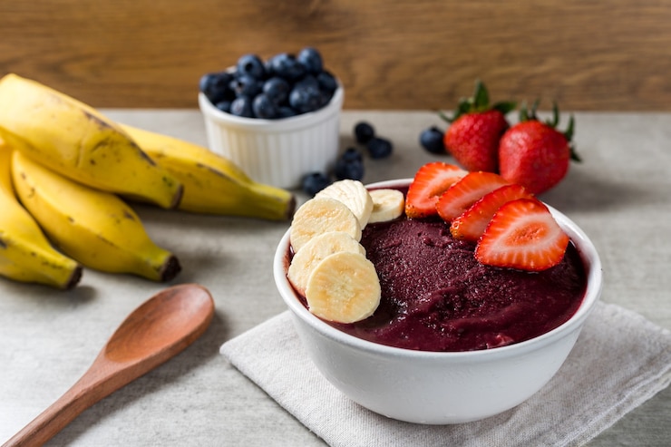 Foto taça de sorvete brasileiro de açaí e congelados com morango e banana. com frutas em fundo de madeira. vista frontal do menu de verão.