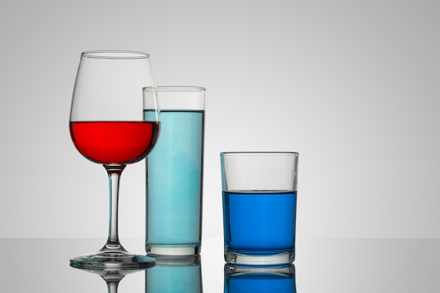 Taça de vidro e taças com fundo branco e bebidas de diversos tipos e cores