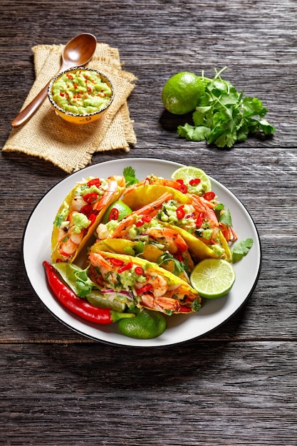 Taco-Schalen mit Garnelen, Kohlsalat, Limette und Guacamole auf einem Teller, vertikale Ansicht