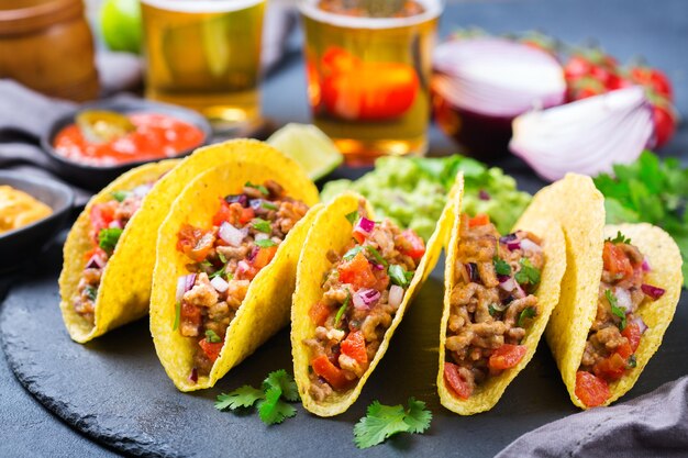 Taco shell e milho tortilla chips nachos com carne moída, picadinho, guacamole, molho de pimenta jalapeño vermelho quente e molho de queijo com tequila ou cerveja em uma mesa.