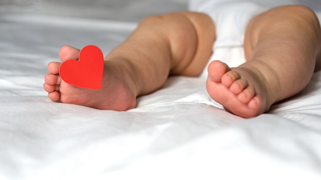 Los tacones de los niños con una etiqueta en el dedo, con un corazón, yacen en la cama sobre un fondo blanco. Día de San Valentín.