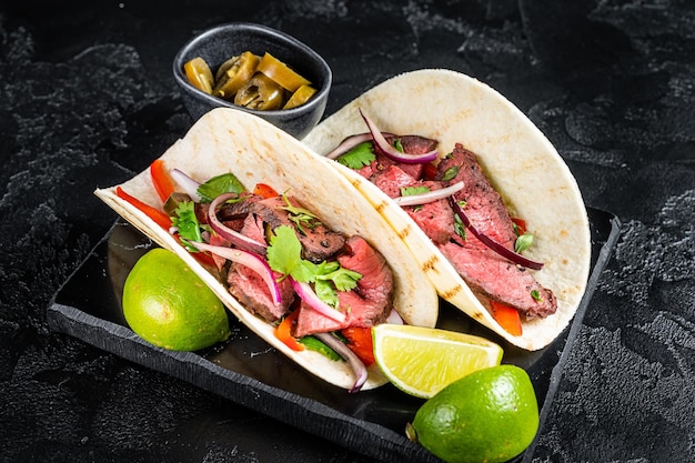 Tacos de bistec mexicano con carne de res cilantro salsa verde jalapeños y cebolla Vista superior de fondo negro