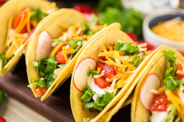 Tacos de carne molida con lechuga romana, tomates cortados en cubitos, rábanos y queso cheddar rallado.