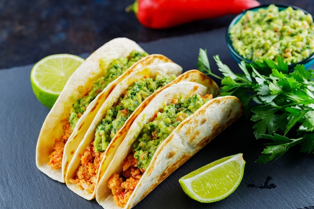 Tacos con carne picada frita y salsa guacamole sobre un fondo oscuro. Tacos e ingredientes mexicanos en una pizarra. Comida hispana