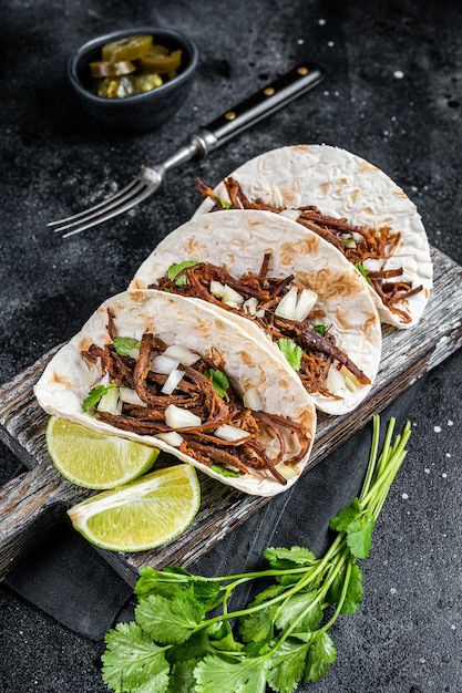 Tacos de carnitas de cerdo en tortillas de maíz con cebolla y lima Fondo negro Vista superior