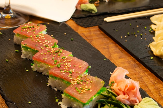 Tacos de sushi com fatias de atum masago ovas sementes de gergelim e cebolinha picada com ginseng em ardósia preta