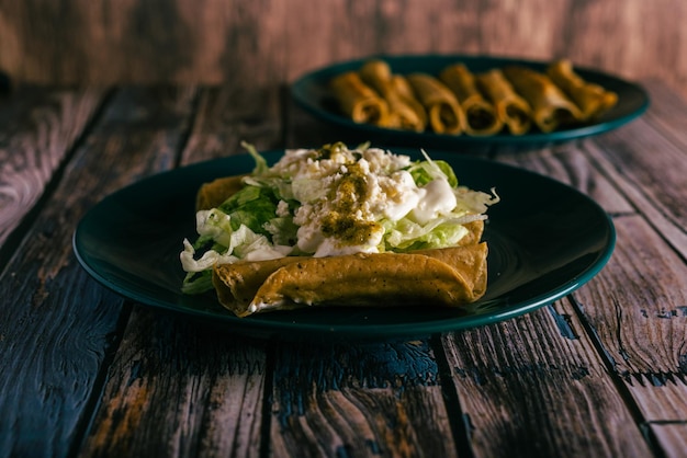 Tacos flauta com creme de queijo e alface em uma mesa de madeira Petiscos mexicanos