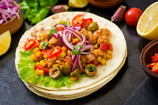 Tacos mexicanos com carne, milho e azeitonas em fundo escuro.