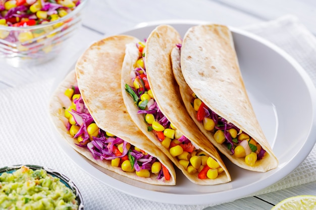 Tacos mexicanos com vegetais diferentes e guacamole em quadros brancos. Tacos vegan com milho, repolho roxo e tomate em um prato branco. Cozinha mexicana