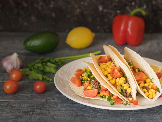 Tacos mexicanos preparados na hora em um prato sobre uma mesa escura com legumes