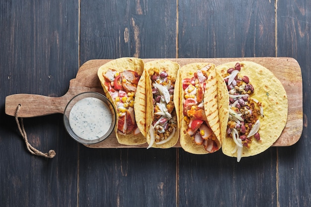 Tacos mexicanos con salsa en una mesa de madera antigua Tacos con frijoles, maíz, cebollas, tomates y carne