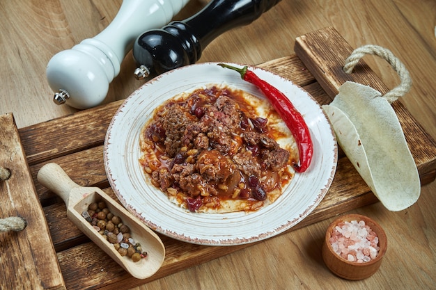 Tacos mexicanos tradicionais com feijão, chili peppers, carne em chapa de cerâmica branca na mesa de madeira. saborosos burritos de carne com chili com carne em tacos de milho