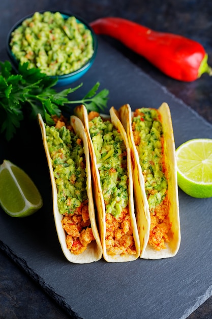 Tacos mit gebratenem Hackfleisch und Guacamole-Sauce auf dunklem Hintergrund. Mexikanische Tacos und Zutaten auf einem Schieferbrett. Hispanisches Essen