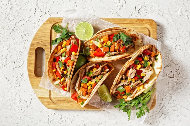 Tacos mit gegrilltem Hühnerfleisch, Mais, gerösteten Süßkartoffelwürfeln, Paprika und Petersilie, serviert auf einem Holzbrett, Nahaufnahme