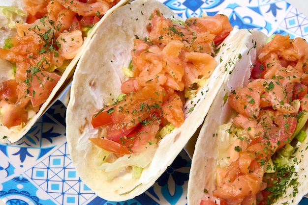 Tacos mit Lachs und Tomate auf einem blauen Teller auf weißem Hintergrund