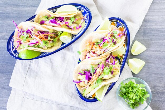 Tacos de pescado fresco con verduras y salsa de guacamole sobre tortillas de maíz blanco.