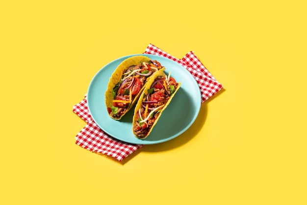 Tacos tradicionales mexicanos con carne y verduras sobre fondo amarillo