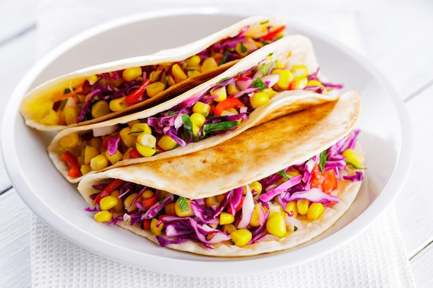 Tacos vegan com milho, repolho roxo e tomate em um prato branco. Tacos mexicanos com vegetais diferentes em quadros brancos. Comida saudável. Cozinha mexicana