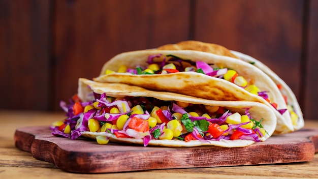 Tacos veganos com vários vegetais em uma tábua de cortar. Tacos com milho doce, repolho roxo e tomate em tábuas de madeira. Copie o espaço