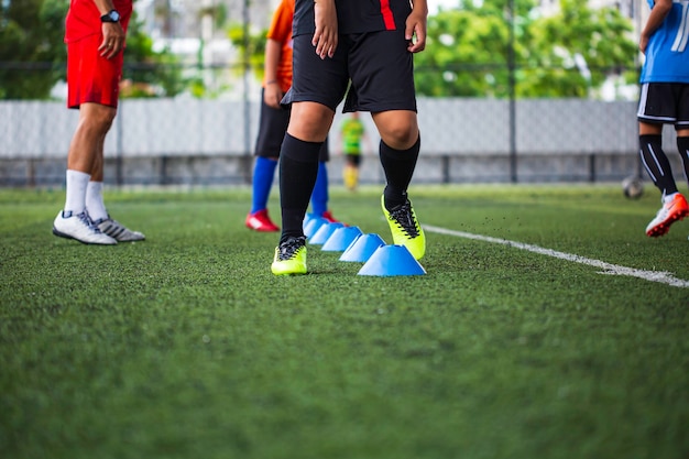 Tácticas de balón de fútbol en el campo de hierba con cono de barrera para entrenar a los niños en la habilidad de salto en la academia de fútbol