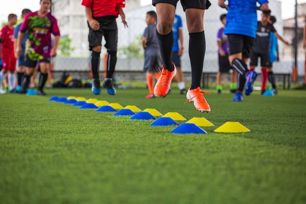 Foto tácticas de balón de fútbol en el campo de hierba con cono de barrera para entrenar a los niños en la habilidad de salto en la academia de fútbol