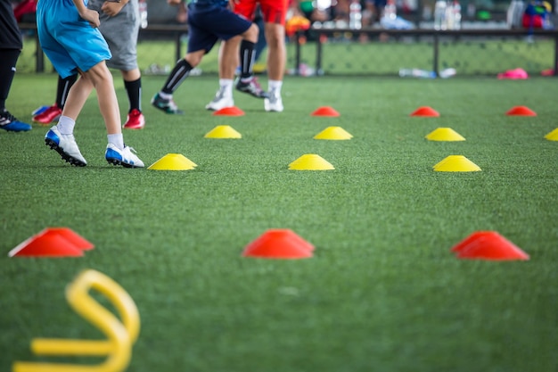 Tácticas de balón de fútbol en el campo de hierba con cono para entrenar a los niños en la habilidad de salto en la academia de fútbol