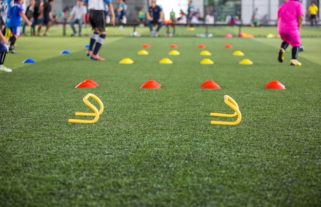 Tácticas de balón de fútbol en el campo de hierba con cono para entrenar a los niños en la habilidad de salto en la academia de fútbol