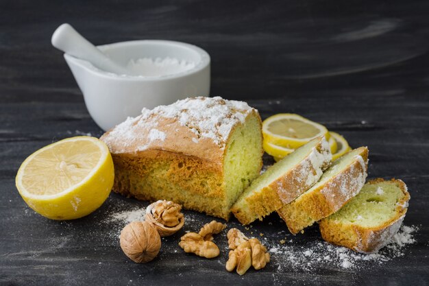 Foto tadelloser kuchen auf schwarzer oberfläche mit zitrone, nüsse