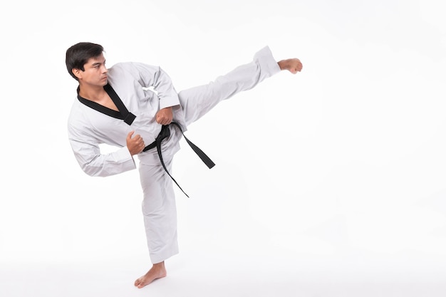 Taekwondo High Kick - Schwarzgurt Taekwondo Athlet Martial Arts Master, gutaussehender Mann zeigt High Kick Pose während des Kämpfertrainings einzeln auf weißem Hintergrund mit Kopierraum