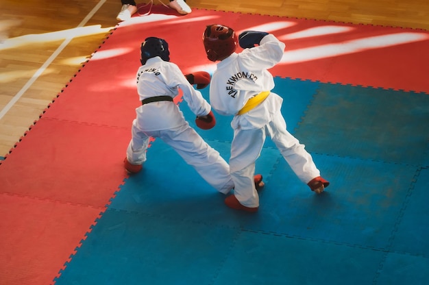 Taekwondo Niños con cascos y guantes kimano tradicionales Duelo deportivo Para la atmósfera, se ha agregado un efecto de ruido de película de desenfoque de movimiento Texto en la chaqueta Taekwondo es el nombre del arte marcial