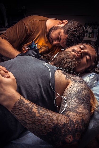 Tätowierer bei der Arbeit im Tattoo-Studio / Mann mit Handschuhen macht Tätowierungsbilder im Salon.