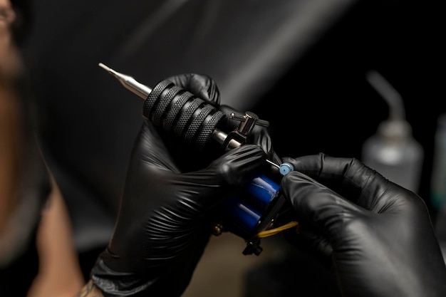 Tätowierer, der seine Tätowiermaschine einrichtet und anpasst, trägt schwarze Handschuhe Body Art Konzept